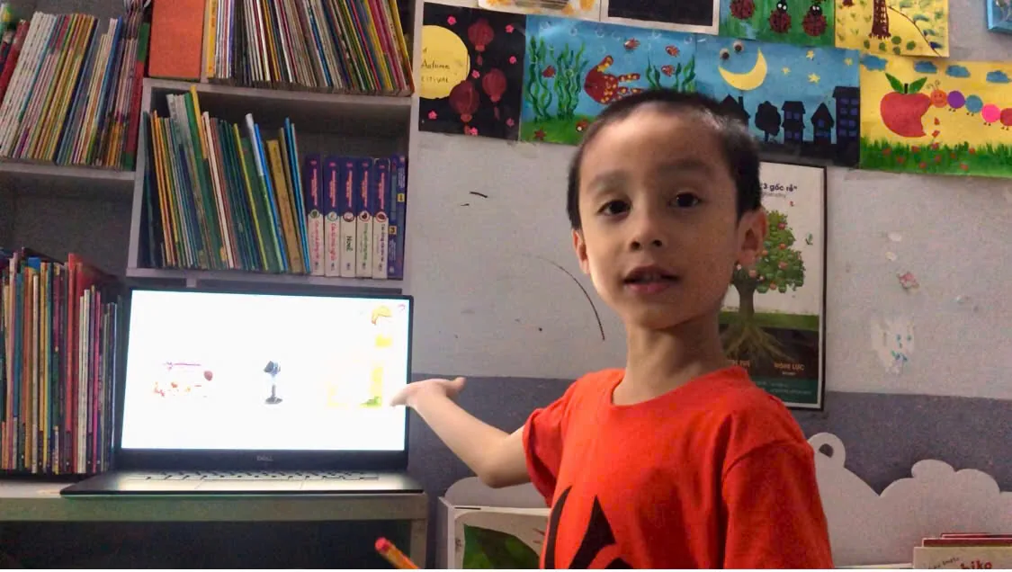Bé học tại nhà bên giá sách, chỉ vào màn hình bài học