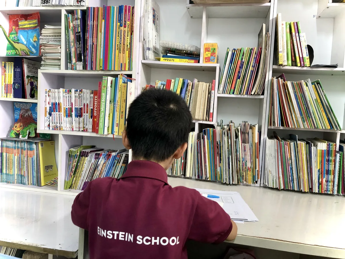 Bé bên giá sách đầy ắp — trong nhà lúc nào cũng có sách